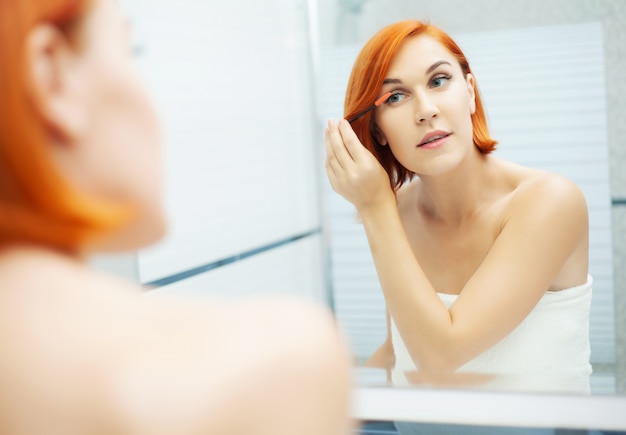 Vrouw met rood haar doet haar make-up