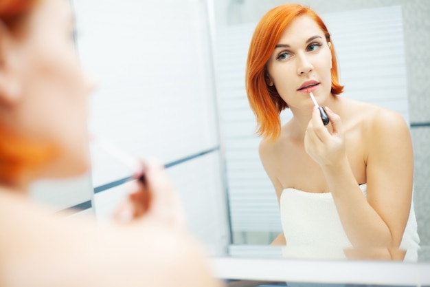 Vrouw met rood haar in de badkamer gebruikt verzorgingsproducten.