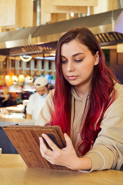 vrouw met rood haar zit in een café werkt op een tablet