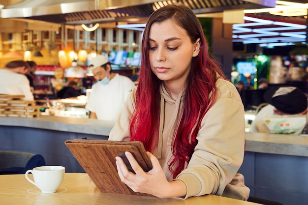 Vrouw met rood haar zit in een café werkt op een tablet
