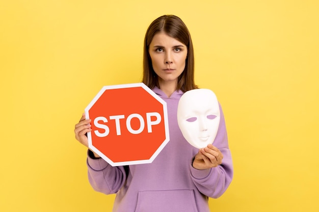 Vrouw met rood stopbord en wit masker kijkend naar camera met strikte bazige uitdrukking