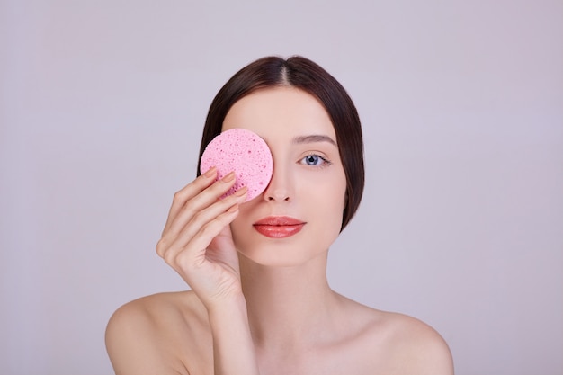 vrouw met roze spons in de buurt van haar gezicht.