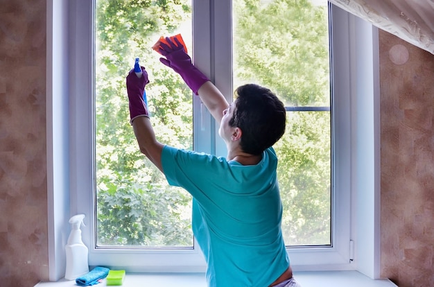 Vrouw met rubberen handschoenen wast raam en houdt raamreinigingsspray in handen. schoonmaakdiensten