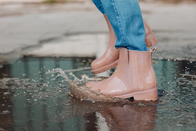 Foto vrouw met rubberen regenlaarzen die rennen en springen in de plas met waterplons en druppels in de herfstregen.