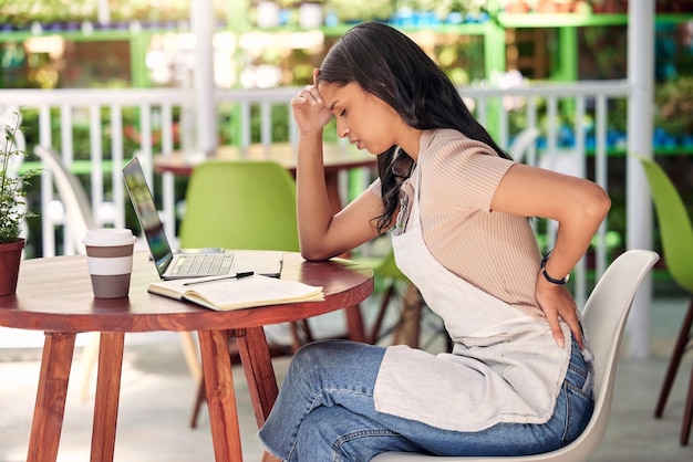 Vrouw met rugpijn laptop in café en stress burn-out met angst en overweldigd aan tafel Geestelijke gezondheid duurzame ondernemer en computer met zorgen, letsel en schulden in openluchtrestaurant