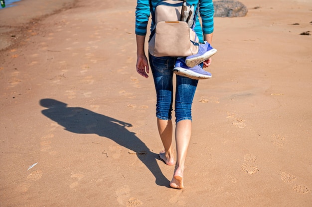 Vrouw met rugzak die blootsvoets op het strand loopt tijdens een zonnige dag achteraanzicht close-up