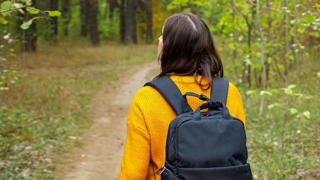 Foto vrouw met rugzak in oranje trui loopt door bos