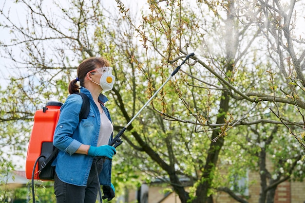 Vrouw met rugzak tuinspuitpistool onder druk bij het hanteren van perzikboom