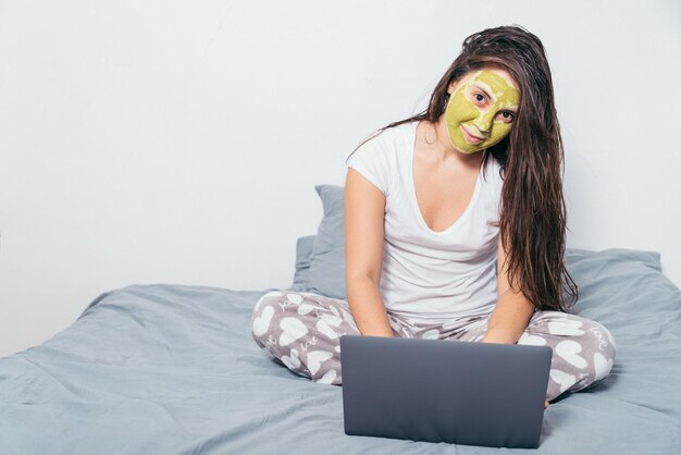 Vrouw met schoonheidsmasker op haar gezicht zit op het bed met nat haar