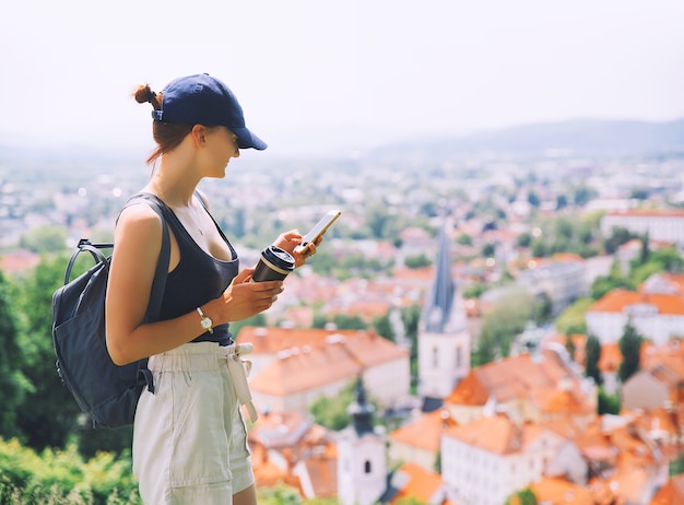 Vrouw met smartphone en koffie in handen op de achtergrond van uitzicht op de stad met rode daken van Ljubljana