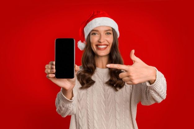 Vrouw met smartphone scherm poseren in Kerstman hoed rode achtergrond