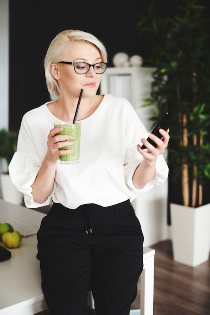 Vrouw met smoothie sms't op het werk