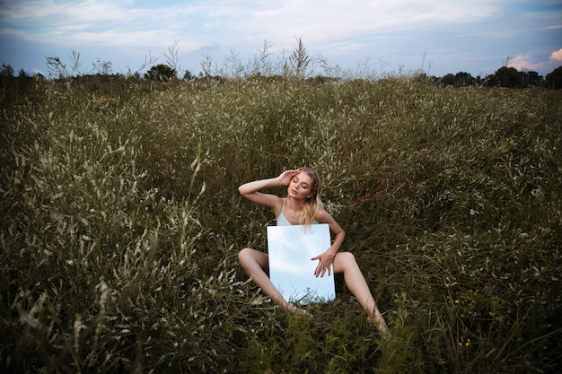 Vrouw met spiegel zit in bloemen bij zonsondergang in de zomer