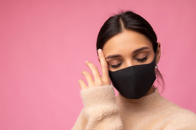 Vrouw met stijlvol beschermend gezichtsmasker, poseren op roze achtergrond. Trendy modeaccessoire tijdens quarantaine van de pandemie van het coronavirus. Close-up studio portret. Kopiëren, lege ruimte voor tekst.