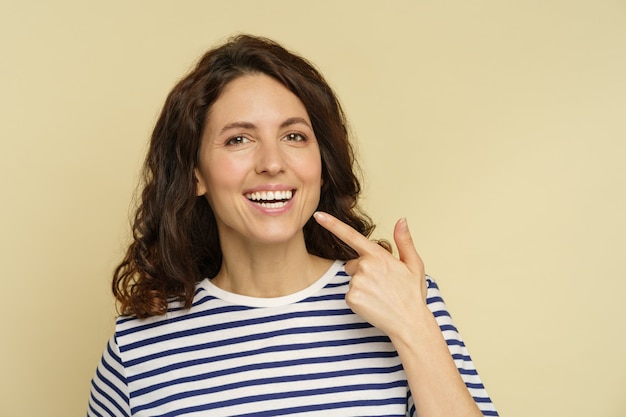 Vrouw met stralende glimlach wijst naar witte gezonde tanden portret van gelukkige vrouw met tandheelkundige gezondheid