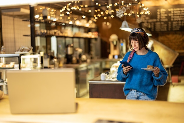 Vrouw met telefoon die haar bestelling bij moderne coffeeshop draagt