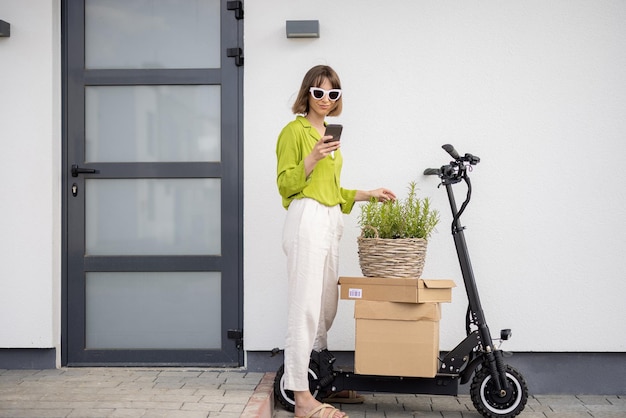 Vrouw met telefoon elektrische scooter en pakketten naar huis