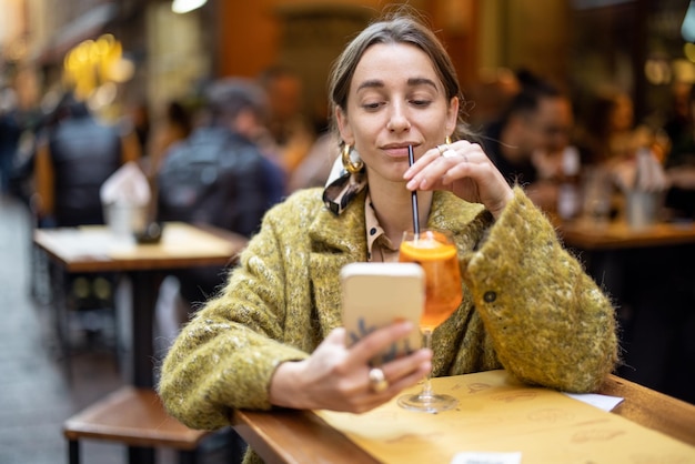 Vrouw met telefoon en drankje aan de bar buitenshuis