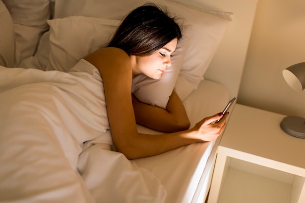 Vrouw met telefoon in bed