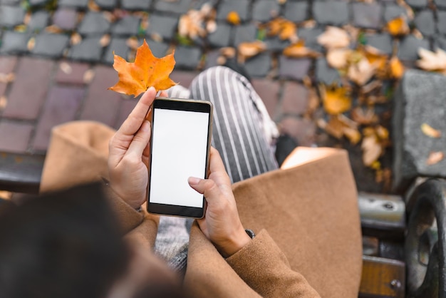 Vrouw met telefoon met wit scherm buitenshuis geel esdoornblad