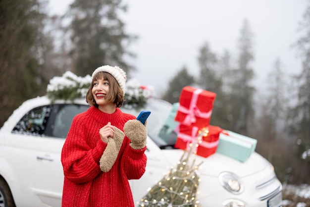 Vrouw met telefoon reizen met de auto ingericht voor kerstmis in de bergen