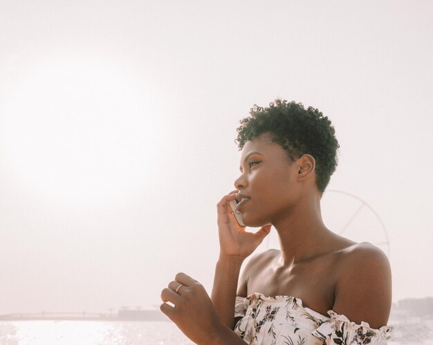 Vrouw met telefoon terwijl ze bij de zee staat tegen een heldere lucht
