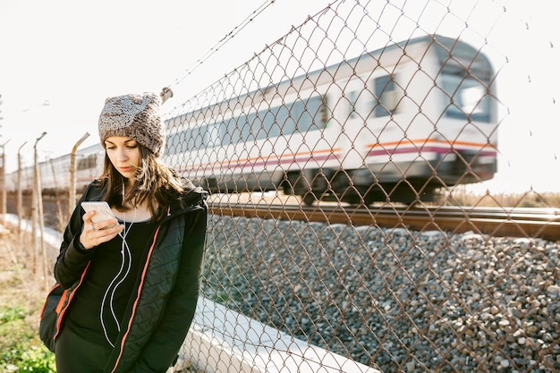Foto vrouw met telefoon terwijl ze bij een hek tegen de trein staat