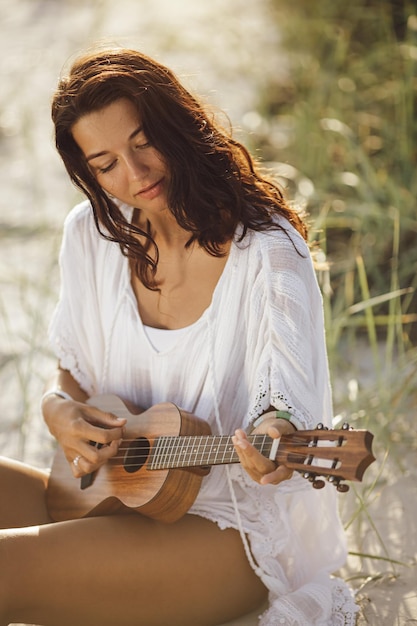 Vrouw met ukelele tijdens de zomervakantie op het strand in de buurt van de zee