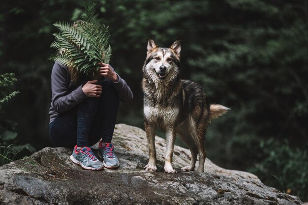 Foto vrouw met varensbladeren terwijl ze met hond op de rots zit