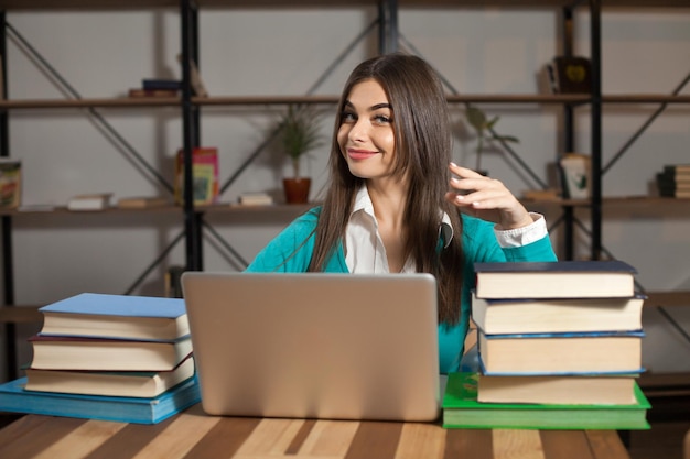 Vrouw met veel boeken en laptop zit aan tafel