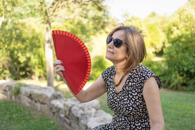 Vrouw met veel warmte die zichzelf frisse lucht geeft met een ventilator in een openbaar park