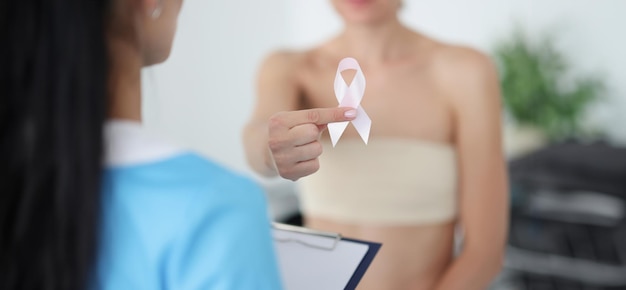 Vrouw met verbande borst die een roze lint vasthoudt bij een afspraak bij de dokter