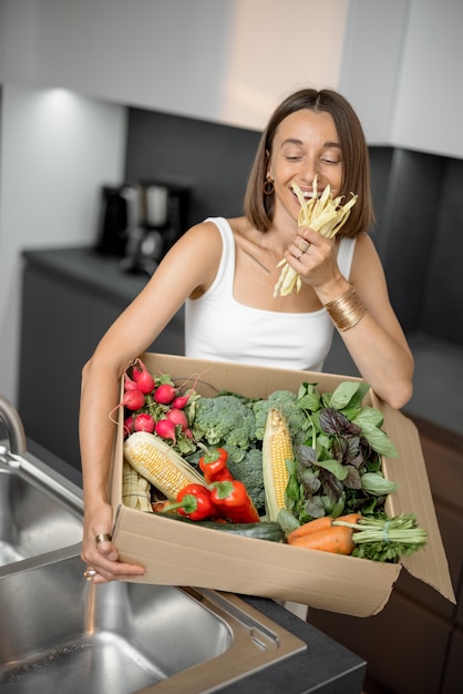 Vrouw met verse groenten verpakt in kartonnen doos in de keuken