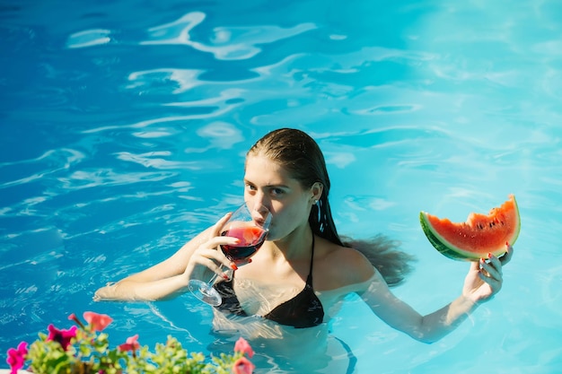 Vrouw met watermeloen en wijn in het zwembad