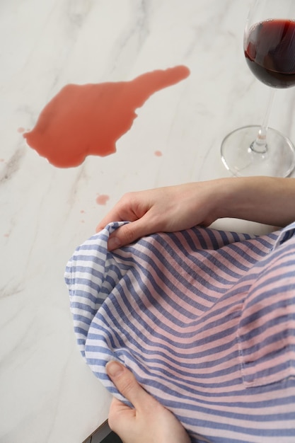 Vrouw met wijnvlek op haar shirt en gemorste wijn aan witte marmeren tafel binnenshuis boven zicht