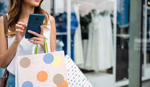 Vrouw met winkeltassen en een mobiele telefoon staat voor een etalage en geniet van het gemak van technologie terwijl ze winkelt naar de nieuwste trends Ze is een moderne consument die sociale media gebruikt