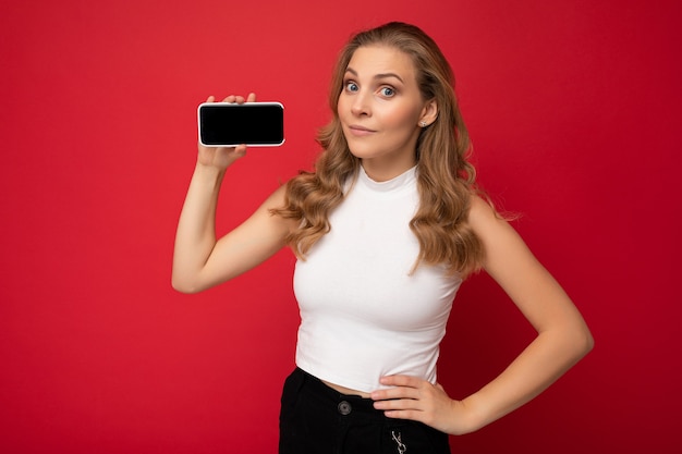 vrouw met wit t-shirt geïsoleerd op rode muur met kopie ruimte met smartphone met telefoon in de hand met leeg scherm.