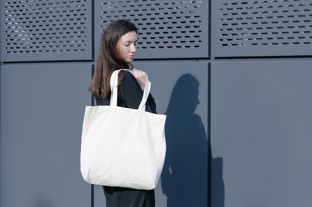 Vrouw met witte textiel eco tas tegen stedelijke stad achtergrond Ecologie of milieubescherming concept Witte eco tas voor mock up