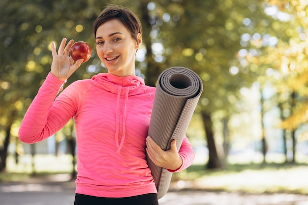 Foto vrouw met yogamat en appel die zich in park bevinden