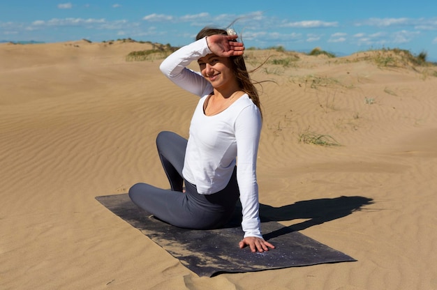 Vrouw met yogamat zittend op duinen