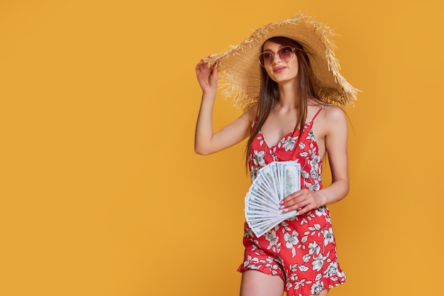 Vrouw met zomerjurk met strohoed houdt een stapel geld in haar handen