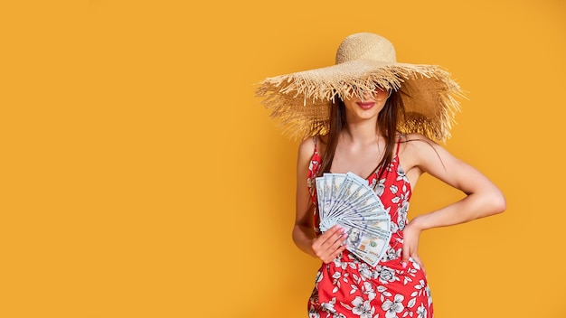 Vrouw met zomerjurk met strohoed houdt een stapel geld in haar handen