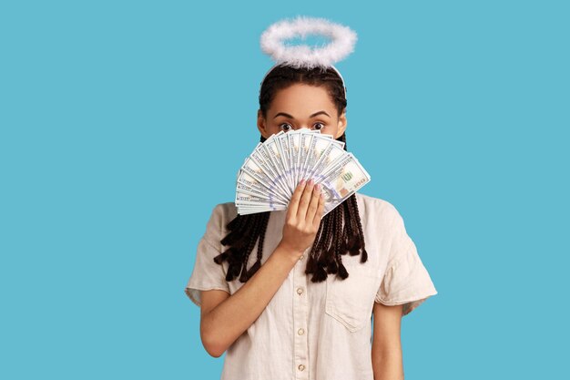 Vrouw met zwarte dreadlocks en nimbus op hoofd die uit dollarbankbiljetten gluren en grote winst verheugen