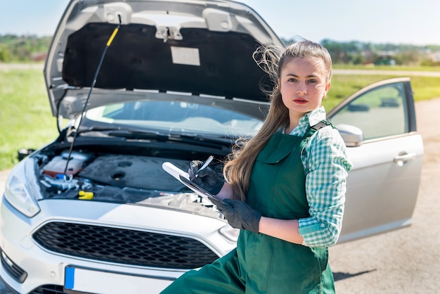 Foto vrouw monteur maakt wat aantekeningen over kapotte auto