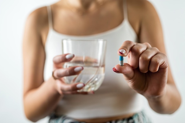 Vrouw neemt cosmetische supplementen voor een stralende huid terwijl ze visoliecapsules en een glas water vasthoudt geïsoleerd op een witte achtergrond vrouwelijke handen capsule en water in een glas