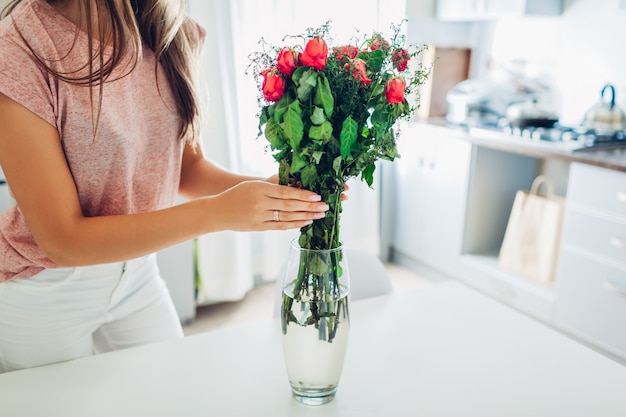 Vrouw neemt dode droge rozenbloemen uit vaas. Huisvrouw die gezelligheid op keuken behandelen.