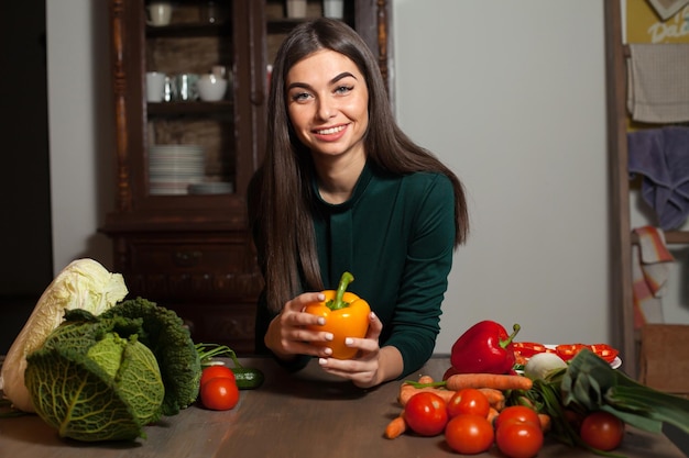 Vrouw neemt een gele paprika in haar handen aan tafel