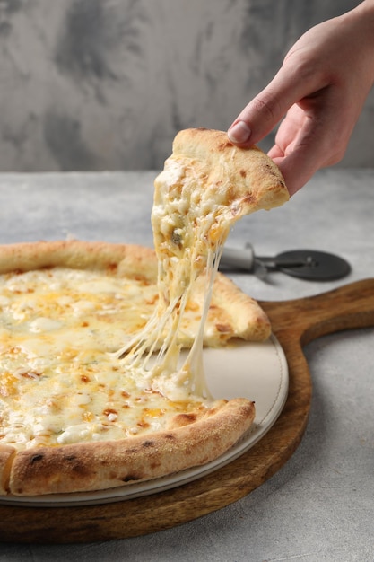 Vrouw neemt een stukje heerlijke kaaspizza bij lichtgrijze tafel close-up