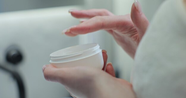 Foto vrouw neemt een witte handcrème uit een witte pot met haar vinger close up skin care huid hydrateren concept