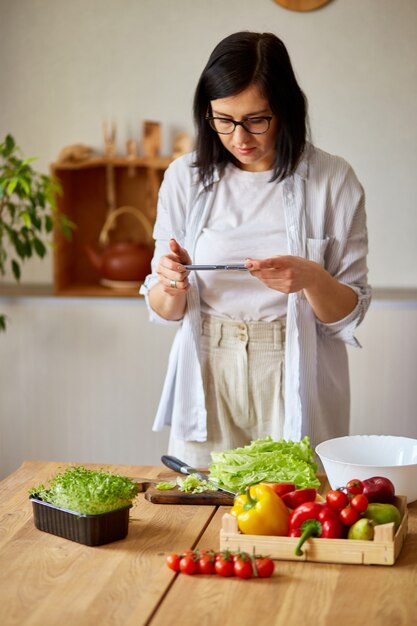 Vrouw neemt foto van gezonde salade met smartphone voor haar blog op keuken thuis